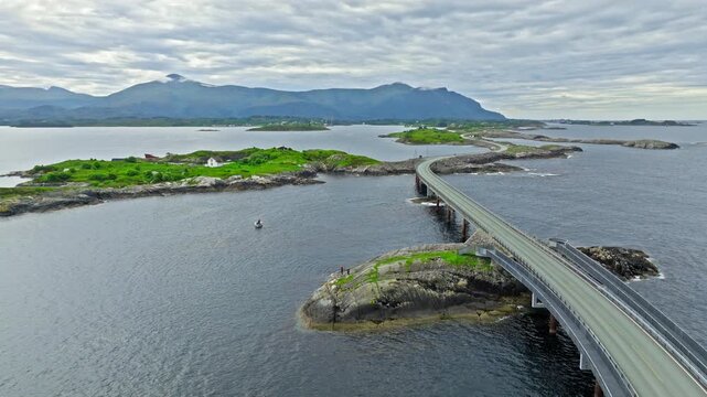 Aerial view of the Atlantic Road (Atlanterhavsveien) in Norway, Norwegian bridge span crossing open water with green islets on both sides . Drone view floats onward, widening the scene.