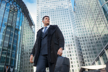 A businessman is walking through a busy city center. He wears a coat and carries a backpack. Tall...