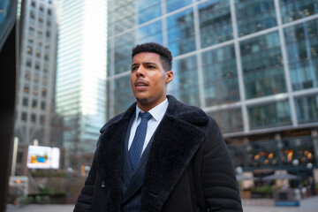 Fototapeta premium A black man walks through a city area filled with tall buildings. He is dressed in formal clothing and appears focused. The time of day looks to be morning or early afternoon.