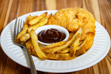 Golden brown air-fried chicken tenders and french fries arranged on a white plate with barbecue dipping sauce on a striped wood grain background.
