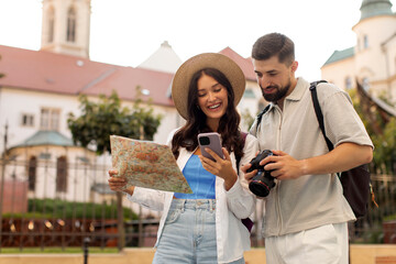 Fototapeta premium Couple exploring city, woman holding map and showing cellphone to man, searching route and location while walking together