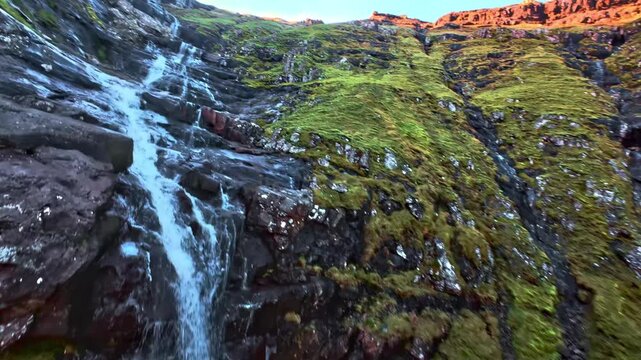 Steep mossy mountain slopewith cascading waterfall oer dark volcanic rocks