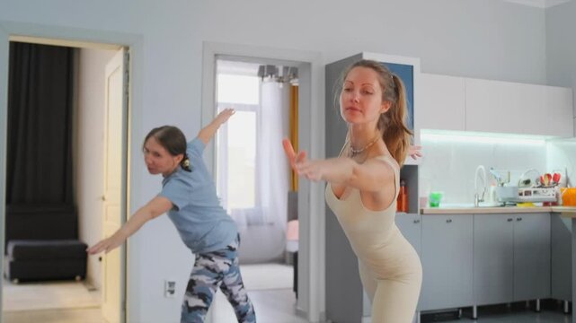 Young yoga teacher with student practicing Warrior II and Triangle poses on mats in a modern apartment kitchen. Concept of healthy lifestyle -  fitness -  posture and balance training indoors.
