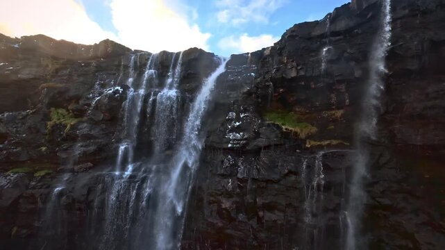 Wide aerial view of multiple waterfalls cascading ove dark textured rock face