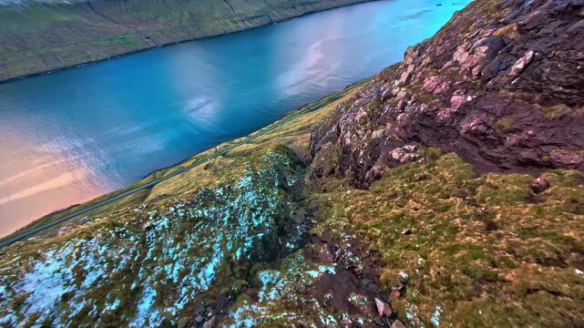 Steep mountain slopes descnding into blue fjord withcoastal road aerial view