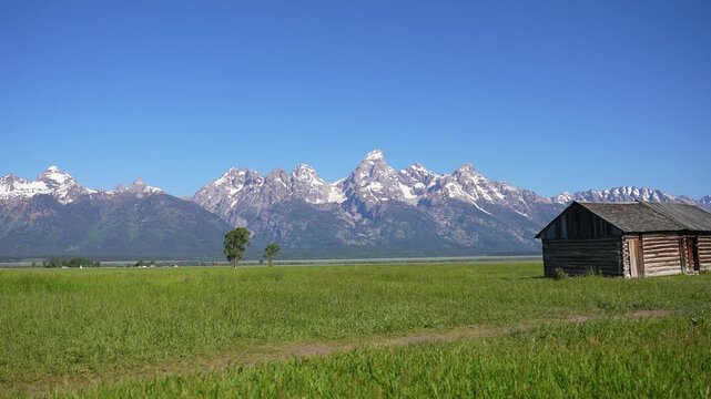 Wide shot of the Grand Teton Mountains with an old barn in the foreground at Grand Teton National Park, Wyoming. Scenic composition combining rustic architecture and majestic alpine peaks, capturing t
