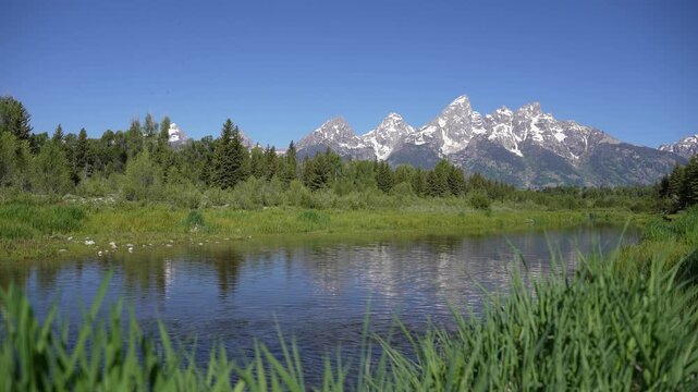 A river flowing in front of the Grand Teton Mountains in Grand Teton National Park, Wyoming. Scenic alpine landscape highlighting moving water, majestic mountain peaks, and serene natural surroundings