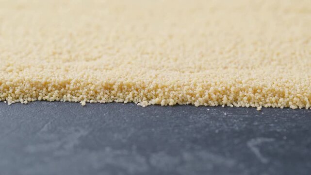 organic couscous on a dark kitchen table.
raw couscous scattered on a black marble background. 