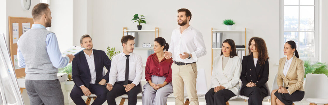 Young business man talking about work project for a group of company employees during a meeting. Confident business people group sitting in a row on conference in modern office. Banner.