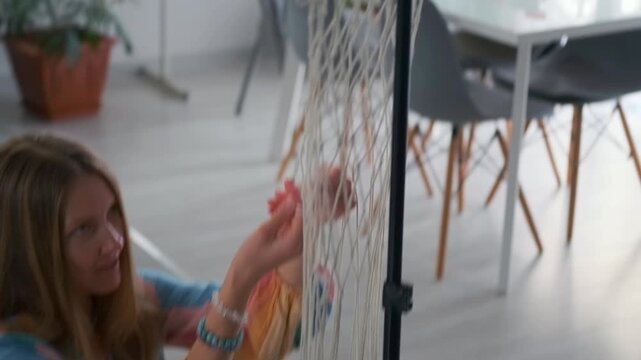 crafting macrame in cozy room -  seated woman customizing colorful macrame wall hanging in modern space -  woman diligently tying complex knots on macrame piece in contemporary dining area with plants