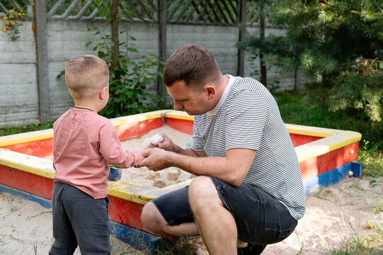 A father wipes his son's hands from the sand after playing in the sandbox