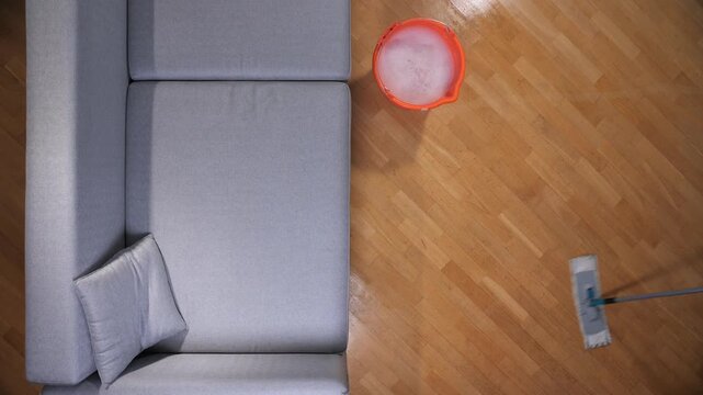 Person is cleaning the parquet floor using a mop and water with detergent from a bucket, keeping the modern apartment tidy and promoting household hygiene with daily chores
