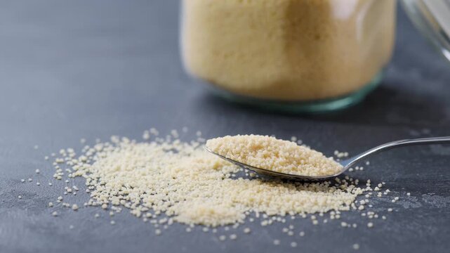 metal spoon with organic couscous on a dark kitchen table. couscous were poured from a glass storage jar into a metal spoon on a dark kitchen table.
