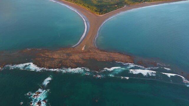 Low altitude drone shot flying backward over the Whale Tail sandbar in Uvita with coastal mountains and the Pacific Ocean in the background.