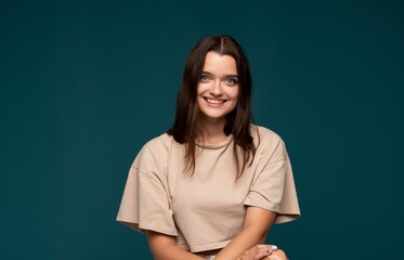 Smiling young woman with natural makeup and brown hair posing against dark green studio background with relaxed and friendly expression