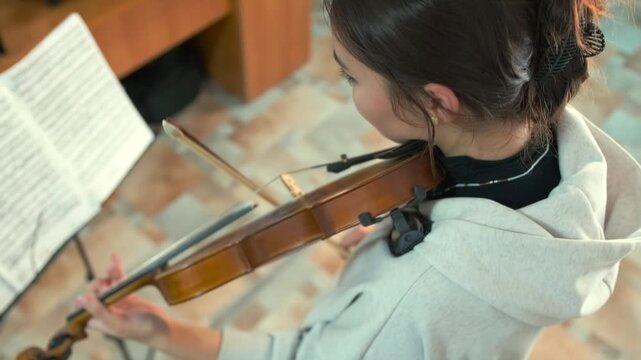Close-up of a serious young woman performing on violin during an audition. She follows sheet music attentively -  demonstrating focus -  classical training and musical maturity under exam conditions.