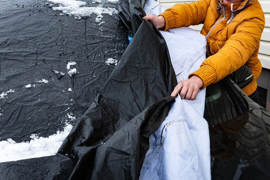 The driver opening the car protected from the weather by a tarpaulin cover in winter.