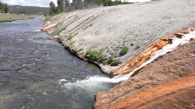 Close-up shot of a geyser mixing with a river at Yellowstone National Park, Wyoming. Detailed view capturing the interaction of steaming hot spring water with the flowing river in a dramatic and sceni