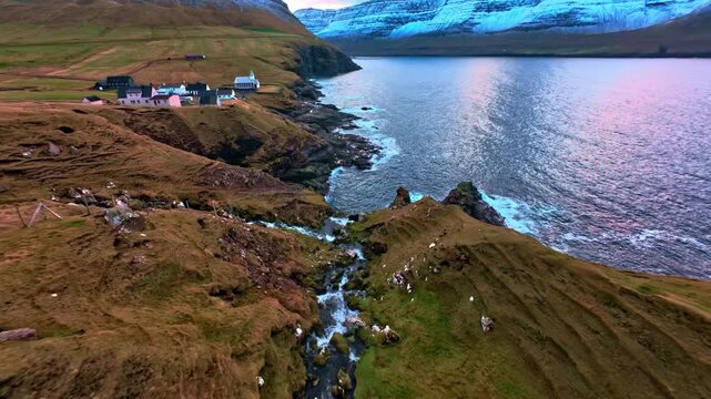 Coastal village on cliff ege with stream flowing int ocean at sunset aerial viw
