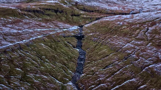 Aerial view of snowy mountin valley with winding stram in rugged terrain