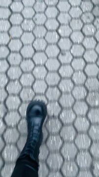 Urban footstep lands on geometric stones, Detailed view of leather boot pressing onto intricately patterned urban pavement tiles during brisk walk Video taken on mobile device.