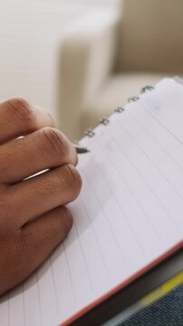 A close-up of a person's hand writing with a pen in a spiral notebook. Vertical video.