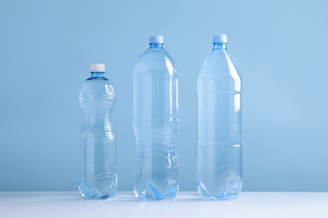 Naklejka premium Water bottles of different sizes on white table against light blue background