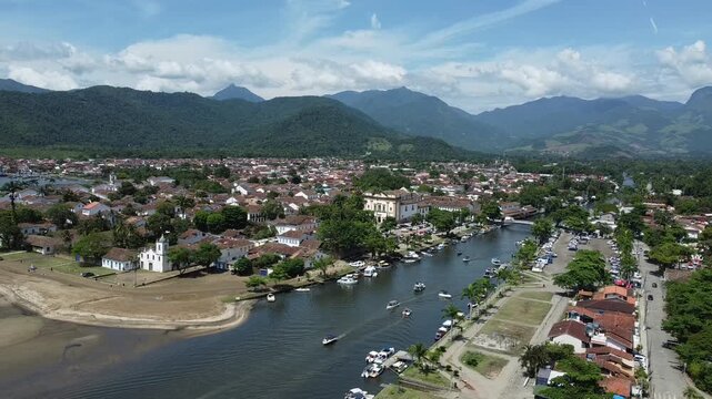 Wide drone shot of Paratys UNESCO historic center with mountains and Atlantic Forest. Captures colonial architecture, the river, and dramatic scenery from above.