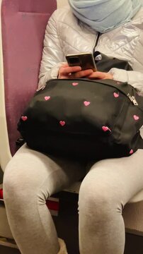 Individual seated with black heart patterned bag and phone in hand, Quiet train scene with passenger holding heartpatterned bag and using their phone Video taken on mobile device.