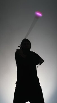 Vertical video of a man's silhouette performing a light show, spinning colorful LED batons. Isolated on a white background.