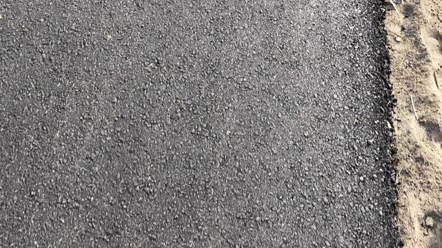 Asphalt road surface with a sandy edge showing texture and color contrast between materials and surroundings
