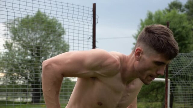 Male shirtless athlete doing push ups on parallel bars at nature. Strong sporty man exercising at sports ground. Young sportsman training hard outdoor. Concept of active sportive lifestyle. Slow mo