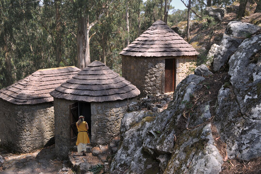 Small round houses built with small stones and thatched roofs, a person in galaic clothes entering one of the houses, medieval atmosphere