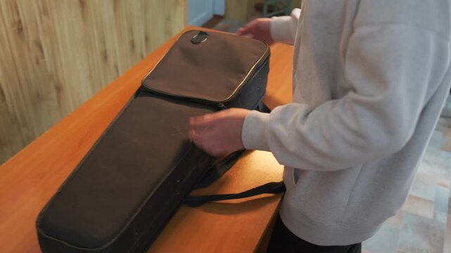 A teenage music student opens a soft protective case and carefully takes out her violin and bow before a rehearsal.