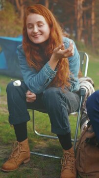 Joyful outdoor moment, Woman appreciates toasted marshmallow beside tent on tranquil evening under twilight glow