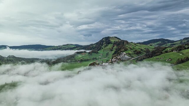 Aerial view of scattered apine village houses on gren hills above fog