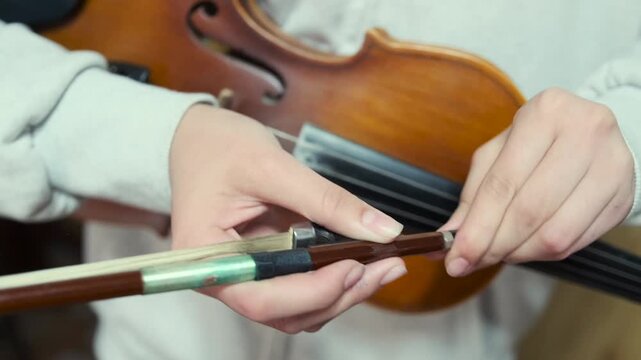 Young Asian violin student hands tightens the bow before rehearsal -  holding a classical violin. Educational environment -  preparation before performance -  focusing on technique and setup.