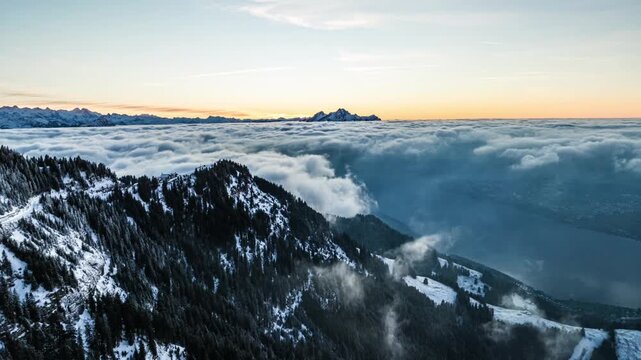Cinematic aerial view of cloud inversion rolling overmountain ridge at sunset