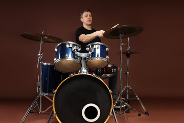Man playing drums with drumsticks on brown background, low angle view