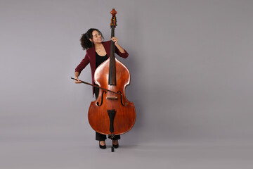 Woman playing double bass on grey background, space for text © New Africa