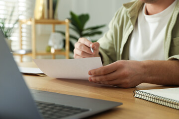 Man writing letter at wooden table indoors, closeup