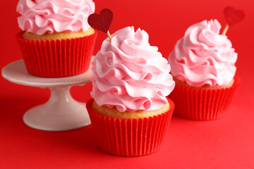 Happy Valentine's Day. Tasty cupcakes with heart toppers on red background, closeup