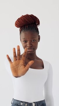 Vertical video of a young African American woman showing a stop gesture with her hand, isolated on a white background.