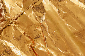 Crumpled gold foil texture with shiny metallic surface, rich reflective details filling entire...