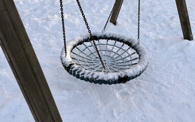 Silent Snowy Swing Against Winter Landscape Scene. Chilly Snowcovered Swing Hanging From Wooden Frame During Winter. Calm Frosty Winter Scene Featuring Abandoned Swing With Textured Ropes
