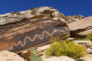 Ancient snake petroglyph carved on desert sandstone rock under clear blue sky, Utah