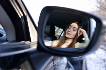 Woman feeling fatigue in her modern auto, view through car side mirror