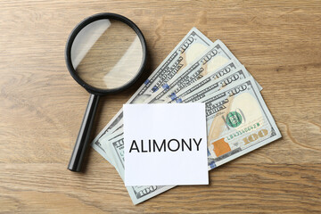 Note with word Alimony, dollars and magnifying glass on wooden table, top view