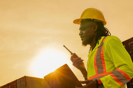 African logistics workers man cheking on site area operations at a busy shipping container yard at sunset. successful coordination in freight, transportation, and supply chain operations