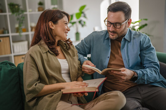 Couple relaxing on sofa together reading books enjoying leisure time